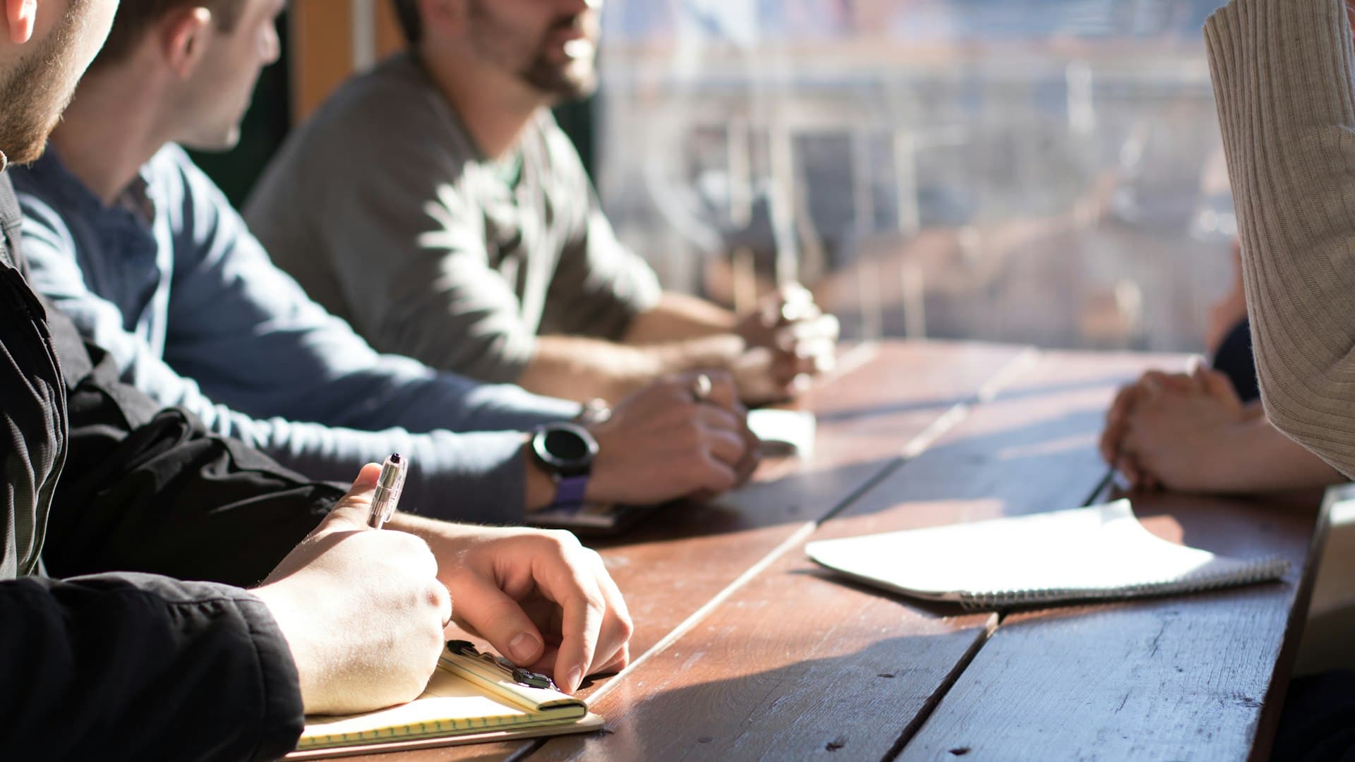 People taking notes around a sunlit wooden table